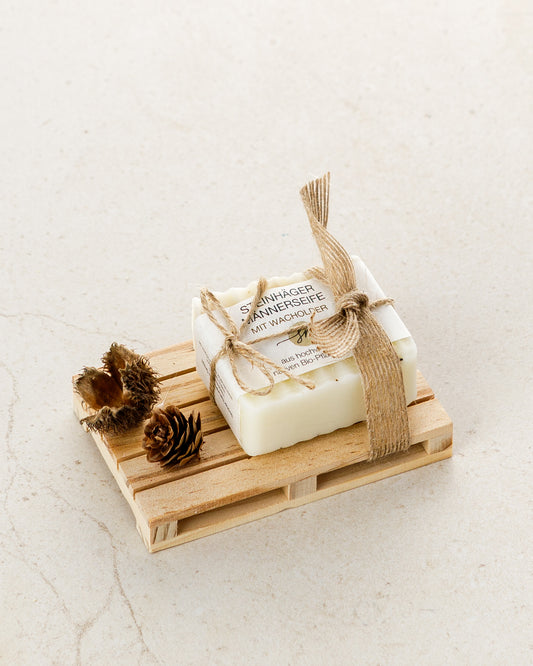 Steinhäger Männerseife auf eine Holz Palette. Als Dekoration wird ein kleiner Tannenzapfen und eine offene Buchecker angebracht und die Seife mit einem Schleifenband befestigt. Ohne Deko