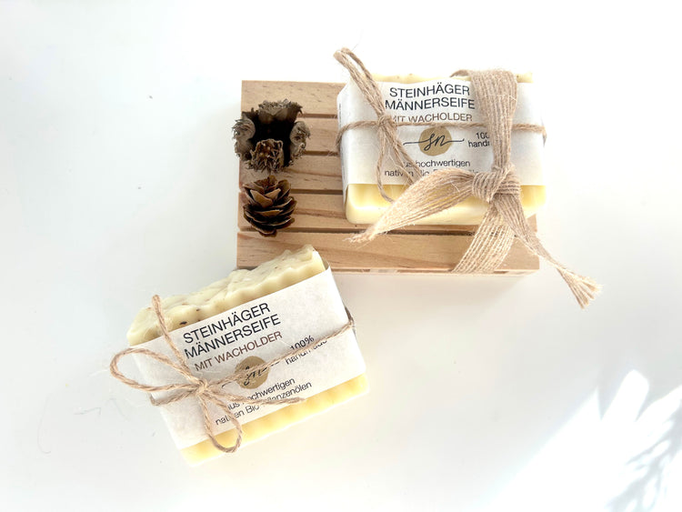 Steinhäger Männerseife auf eine Holz Palette. Als Dekoration wird ein kleiner Tannenzapfen und eine offene Buchecker angebracht und die Seife mit einem Schleifenband befestigt. Ohne Deko von oben mit einer 2. Seife